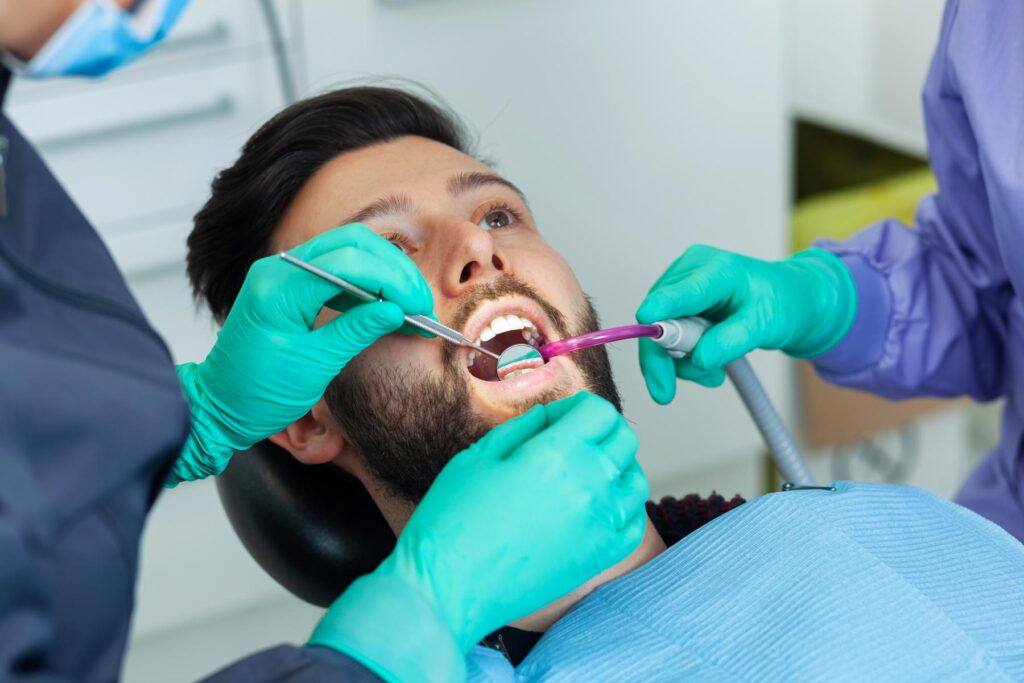 dentist examines a male patients teeth during routine dental check up